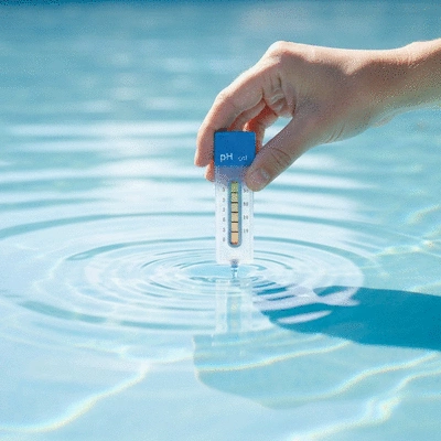 Une main testant l'eau de la piscine avec un kit de test de pH, montrant des résultats clairs et une eau limpide.