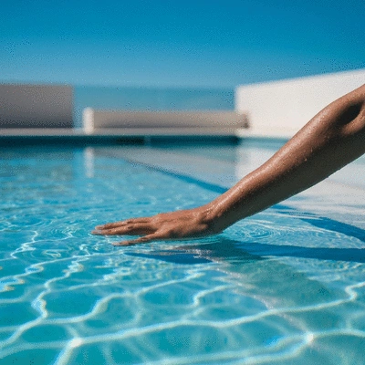 Une main testant la clarté de l'eau d'une piscine avec un ciel bleu et un environnement propre en arrière-plan.